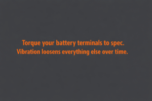 
Minimalist vector graphic with gunmetal background and bright orange text reading “Torque your battery terminals to spec. Vibration loosens everything else over time.”
